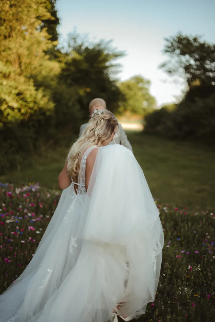 Braut im Tüllkleid geht durch eine Blumenwiese
