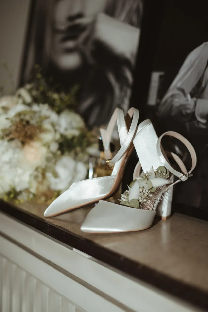 Weiße Brautschuhe mit Trockenblumen neben dem Brautstrauß