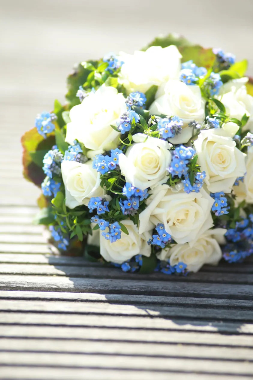 Brautstrauß aus weißen Rosen und blauen Vergissmeinnicht auf Holz