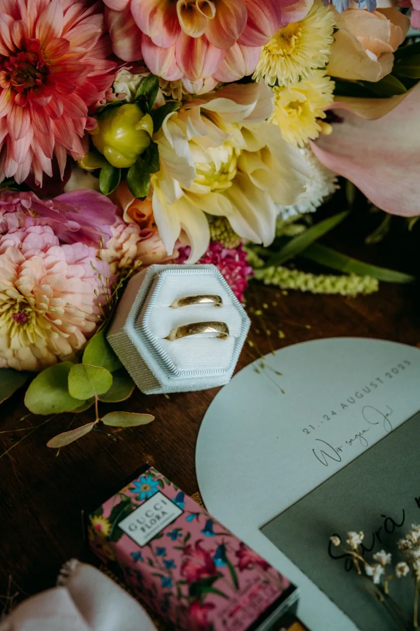 Goldene Eheringe in der Ringbox neben Blumen
