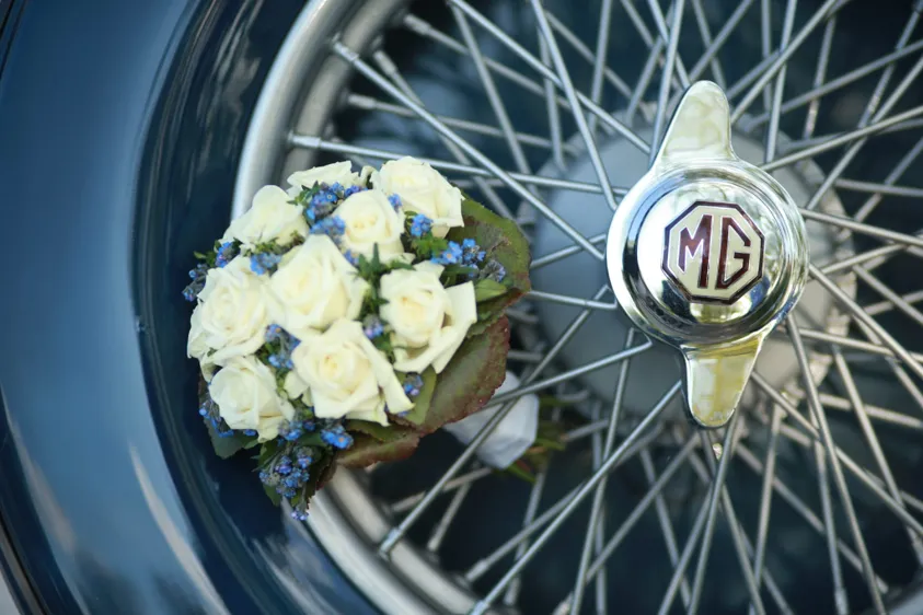 Brautstrauß aus weißen Rosen am Speichenrad eines blauen Oldtimers