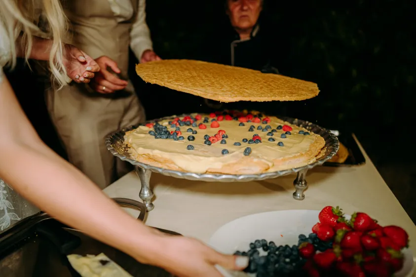Braut richtet Hochzeitstorte mit Beeren und Sahne im Abendlicht an